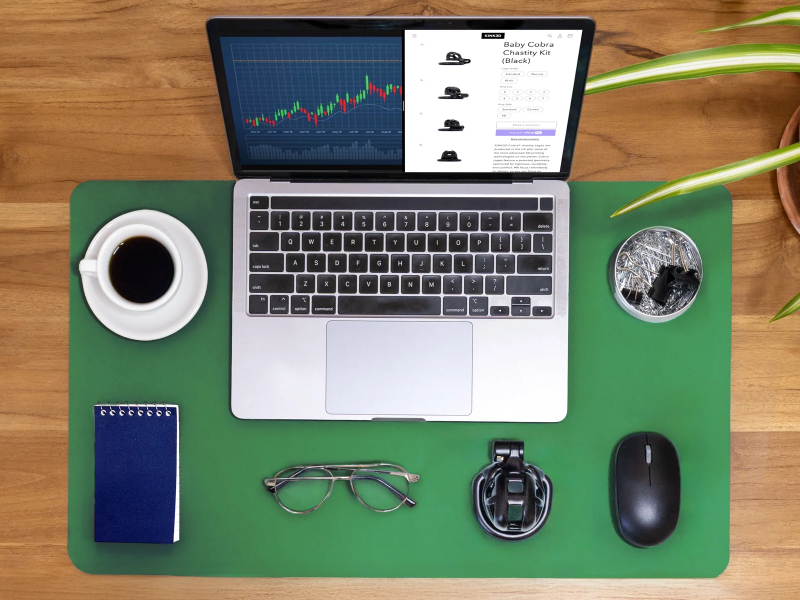 Lifestyle image showing a desk with laptop, glasses, etc - but the standout is the KINK3D Chastity Device. Showing this is part of a normal, consenting adults lifestyle.